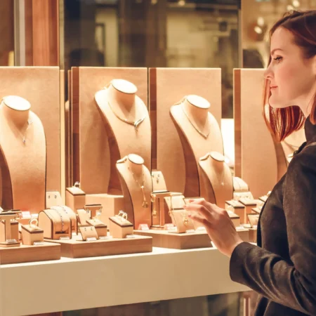 Vrouw bewondert sieraden achter een glazen display in een verlichte winkel.