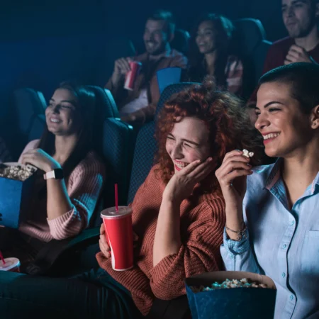 Groep mensen lachend in een bioscoop met popcorn en frisdrank.