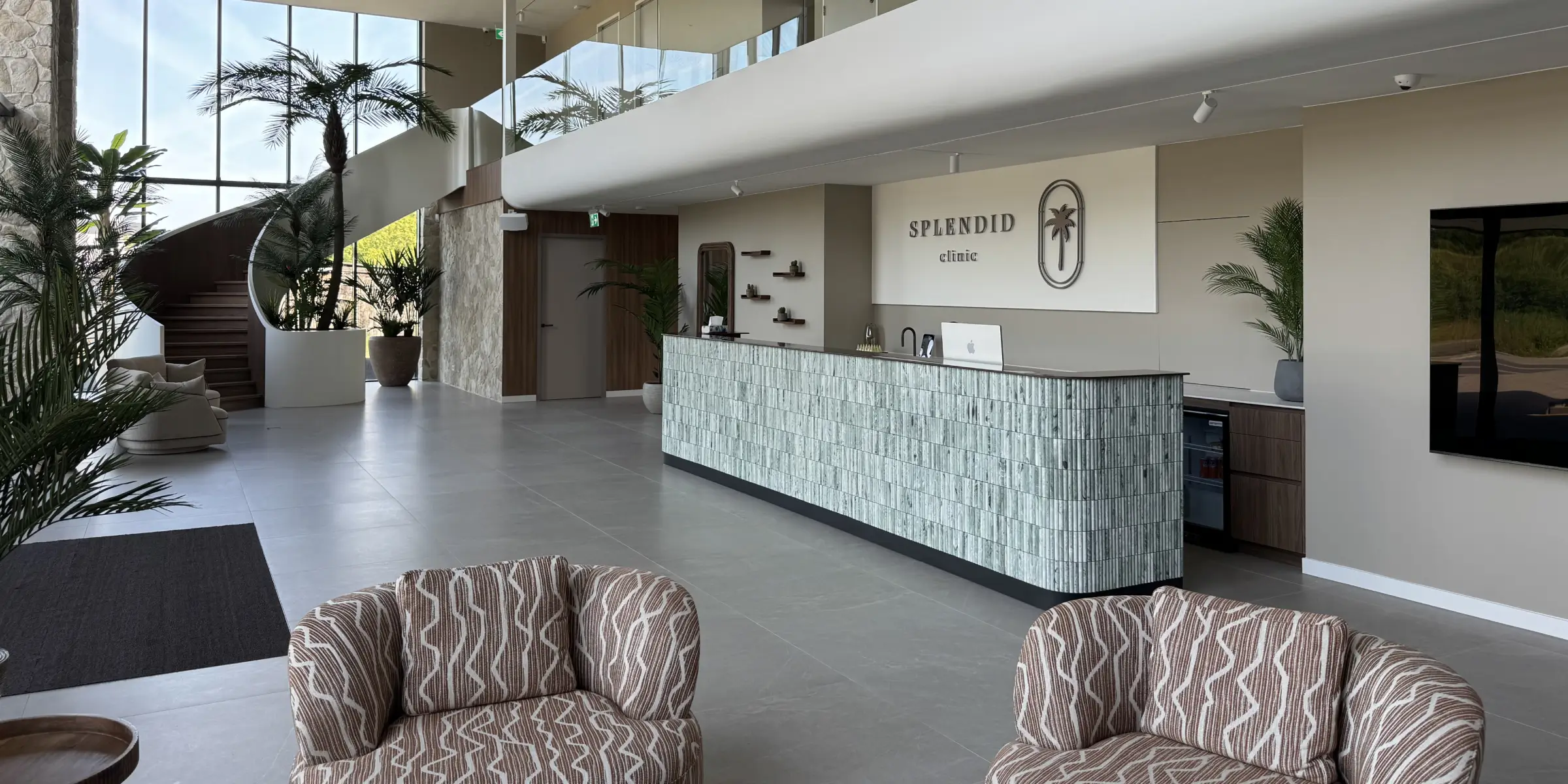 Ontvangstbalie van splendid clinic in een lichte, stijlvolle hal met ronde trap en veel groen