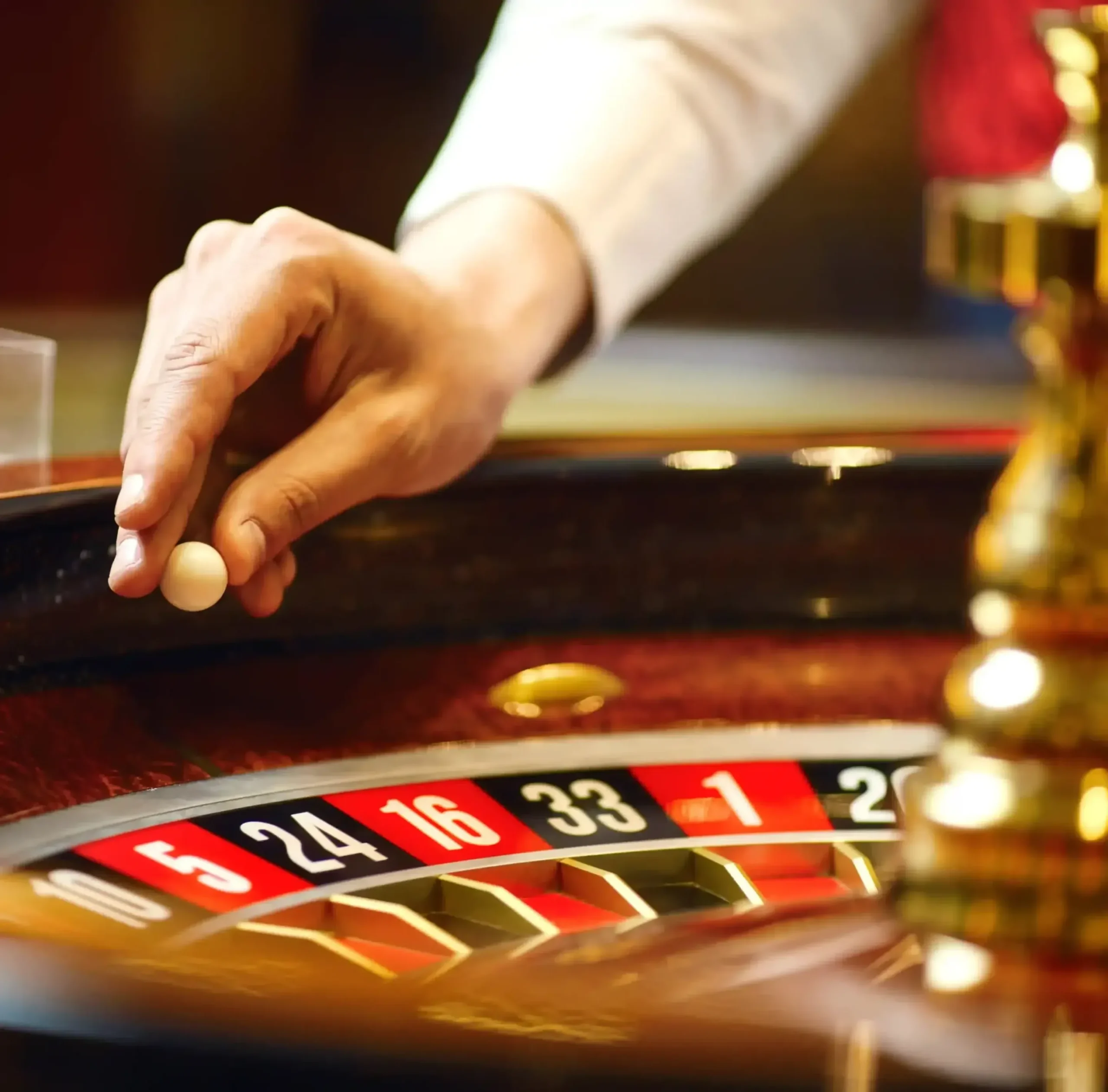 Roulette tafel met croupiershand die de bal draait, rood verlichte casinovloer op de achtergrond.