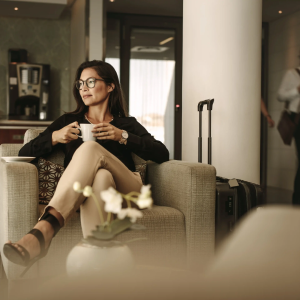 Vrouw ontspant met een kop koffie in de hotellobby met koffer naast zich