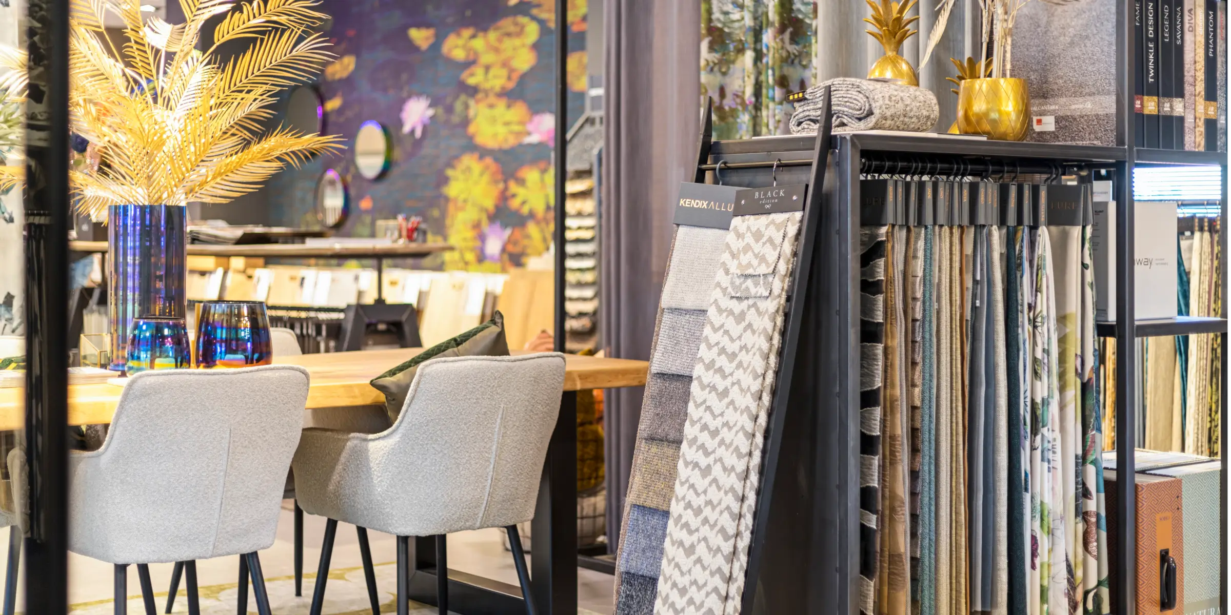 Gezellige showroom met houten tafel, grijze stoelen, kleurrijke decoratie en een stoffenrek – geurmarketing in showroom versterkt de sfeer.
