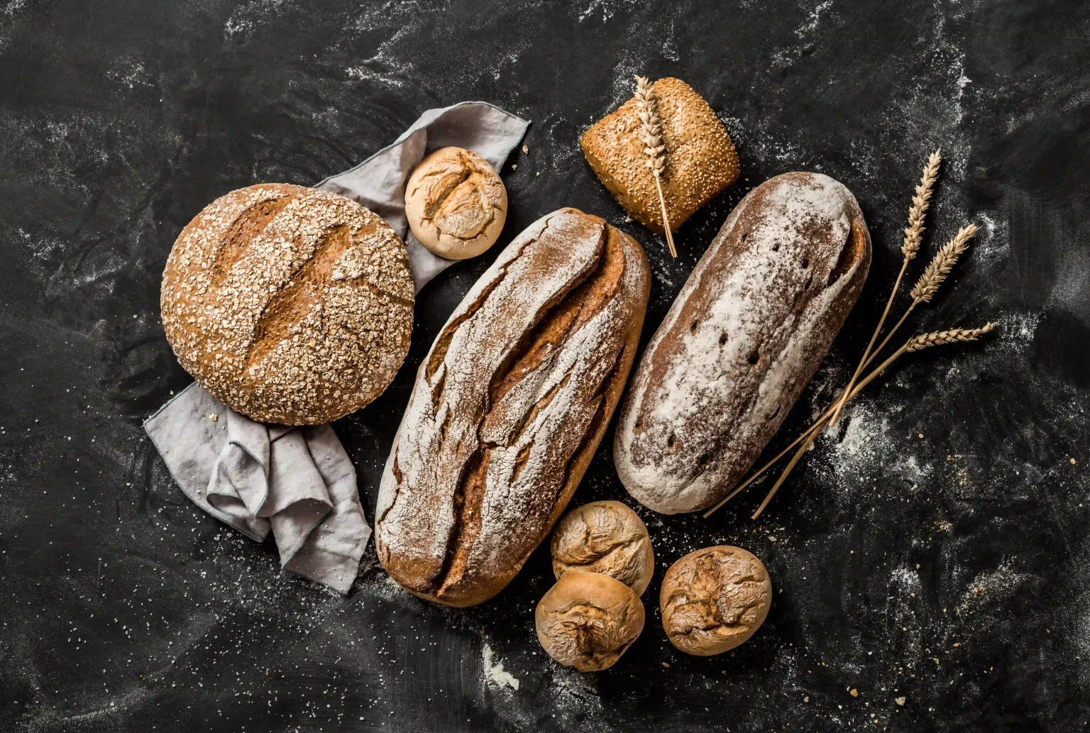 Stilleven van verschillende versgebakken broden met aren op een donkere ondergrond; de geur van “baked bread” roept huiselijke herinneringen op.