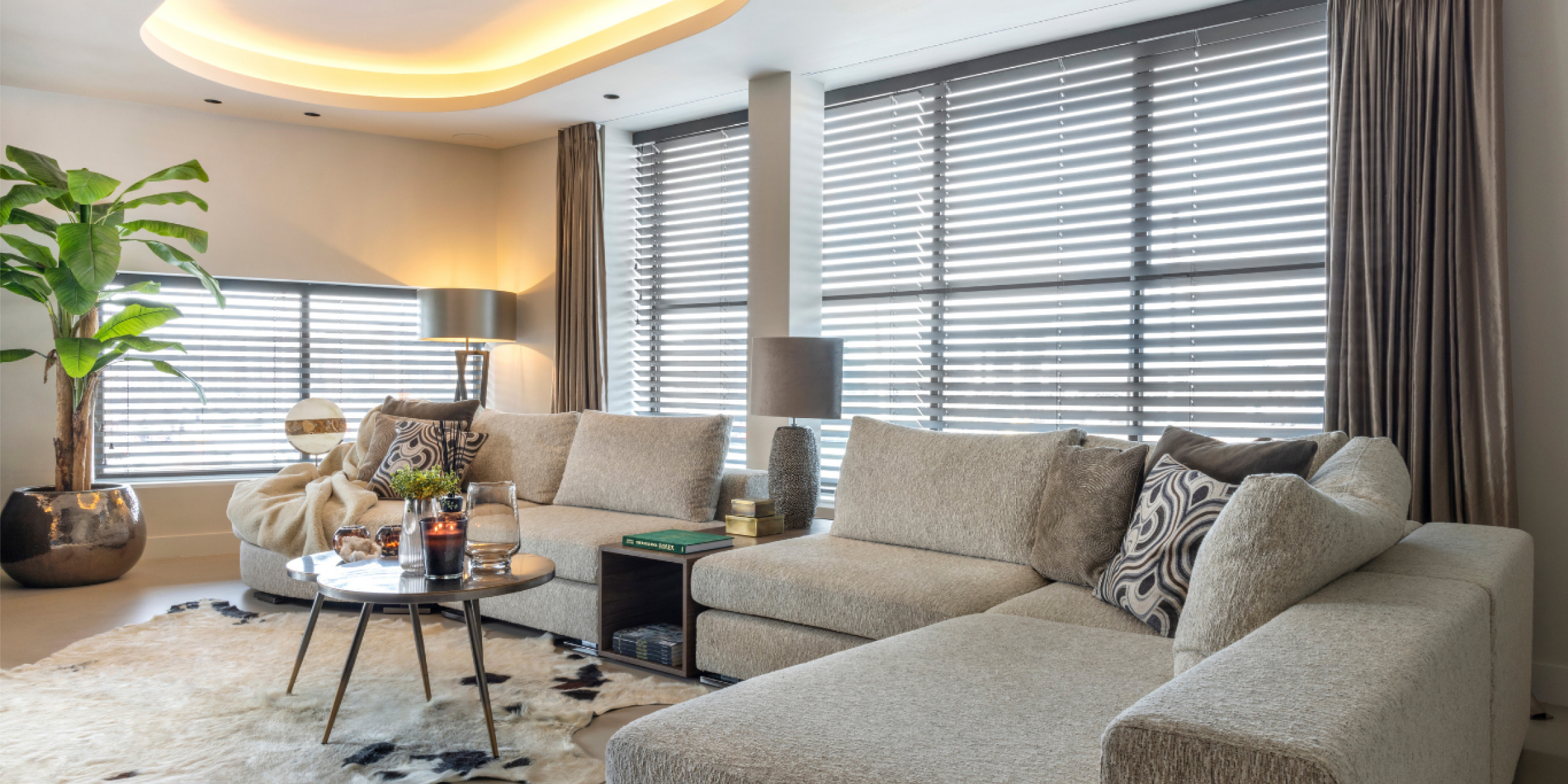 Warm en modern wonen bij interieur corner wateringen | allsens b. V. Moderne woonkamer van interieur corner wateringen met lichte hoekbank, sfeerverlichting en grote ramen met jaloezieën in een warme en stijlvolle setting.